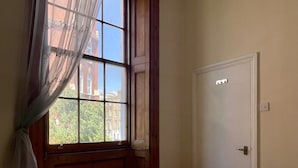 A hotel room with a large window, a bed with white linens, and a door with a light switch. - Baker Street Apartments (London)