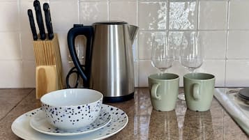 Una encimera de cocina con una cafetera, dos tazas, un bol con plato y un bloque de cuchillos.