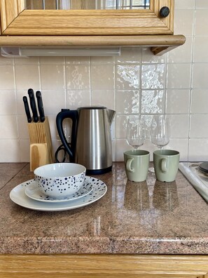 A kitchen counter with a coffee pot, two mugs, a bowl with a saucer, and a knife block. - Baker Street Apartments (London)