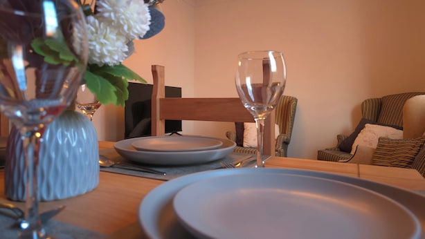 A dining table set with plates and a wine glass, a vase with flowers, and a chair. - Shefford Serenity Apartment In The Heart of Town (Shefford)
