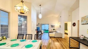 A spacious dining area with a long table set for four, a kitchen area with a black countertop, and a living room with a sofa and a coffee table.