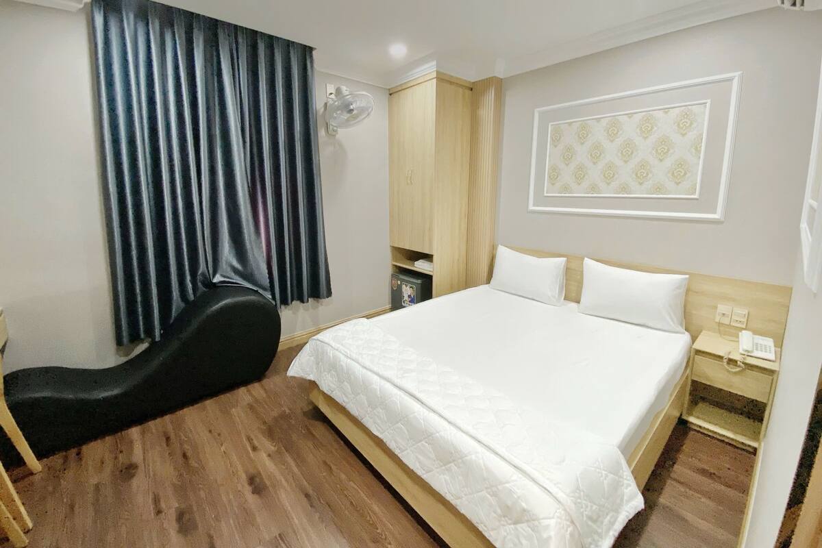 A hotel room with a bed, bedside table, lamp, and a large window with curtains.