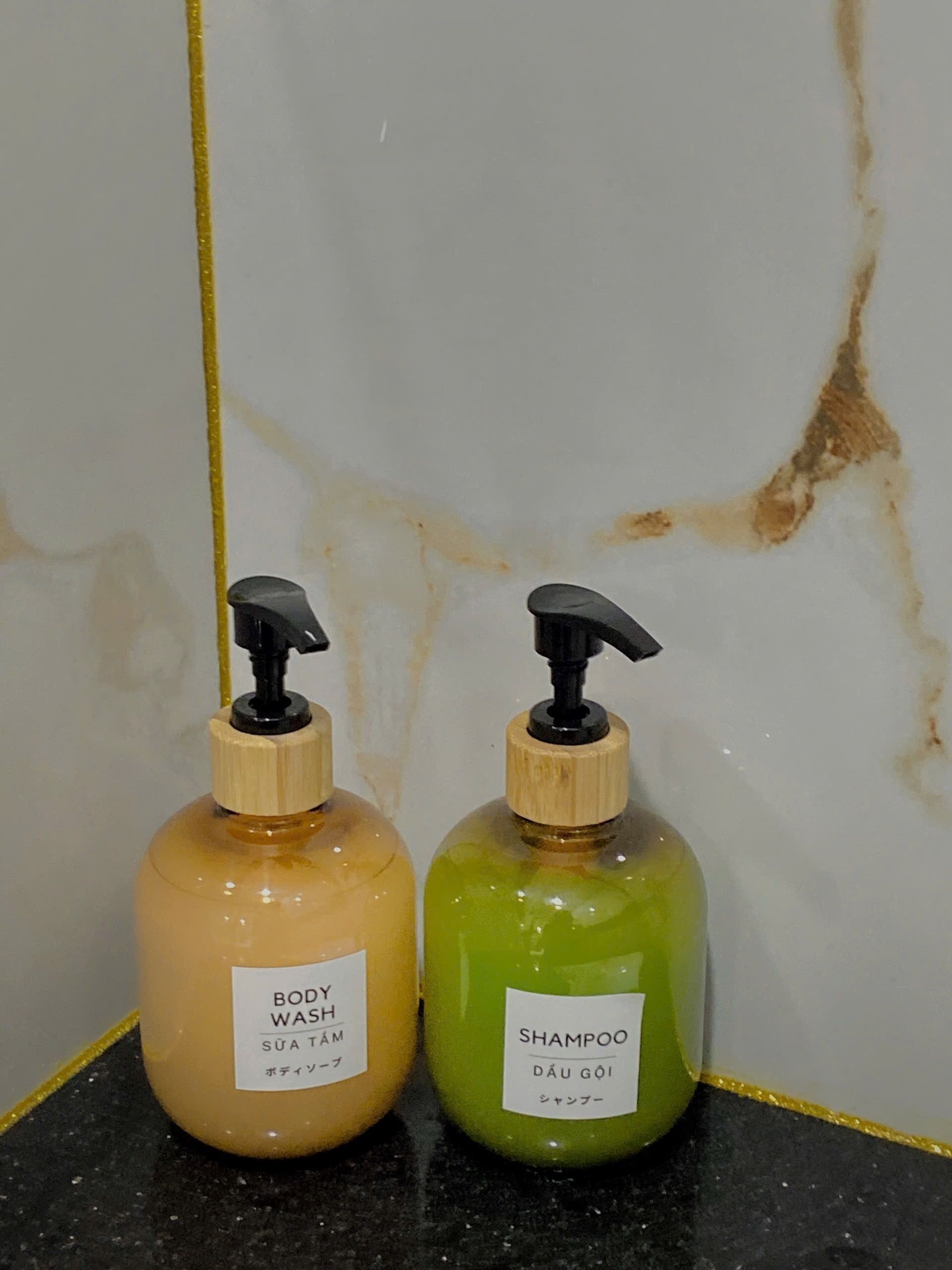Two bottles of body wash and shampoo on a black countertop against a white wall with a yellow line.