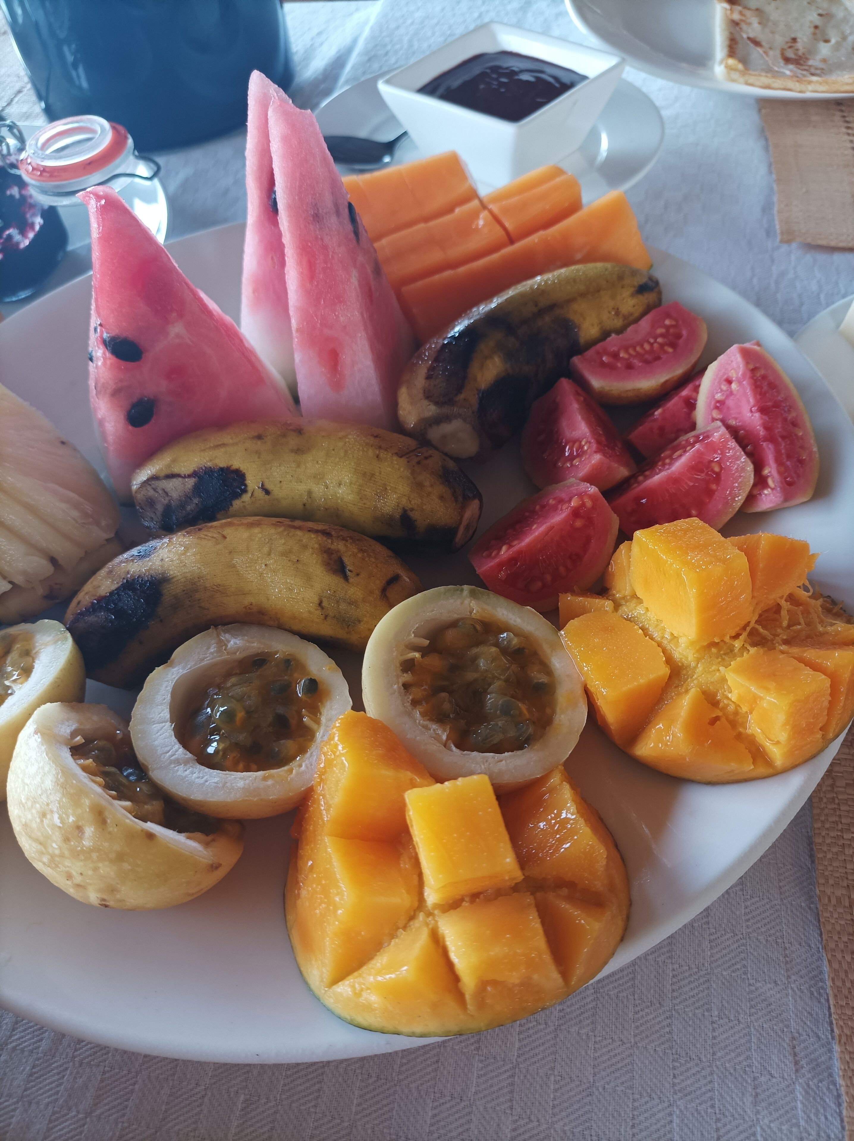 A plate of assorted fruits including watermelon, mango, banana, passion fruit, and papaya.