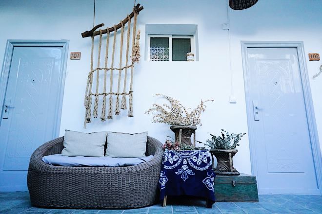 A room with a wicker sofa, a small table with a patterned tablecloth, a macramé wall hanging, and two doors with numbers 101 and 102.