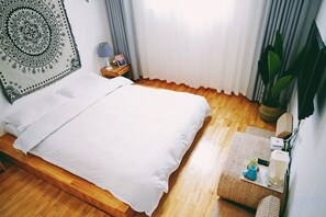A room with a bed, a bedside table with a lamp, a wall tapestry, a potted plant, and a window with curtains. - Dali Yunmu Inn (Dali City)