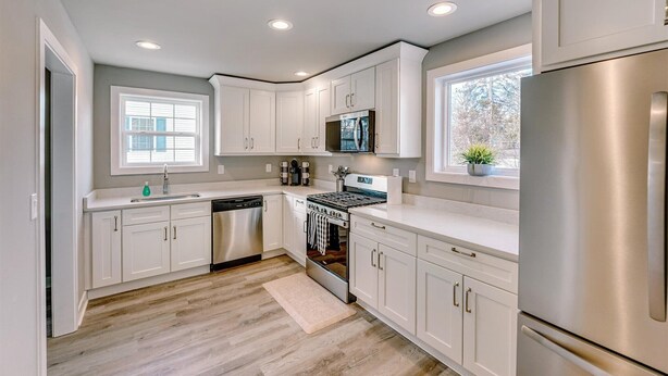 A modern kitchen with white cabinetry, a stainless steel refrigerator, a built-in oven, and a window providing natural light. - Charming Voyage: Ypsi & AnnArbor (Ypsilanti)