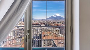 A view from a window with a metal railing, overlooking a cityscape with buildings and a mountain in the distance. - Timeless (Naples)