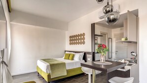 A modern hotel room with a bed, a desk with a chair, a mirror, and a decorative wall piece. - Timeless (Naples)