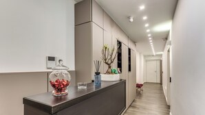 A modern reception area with a dark reception desk, a glass container with red items, a small vase with a plant, and a wall-mounted digital display. - Timeless (Naples)