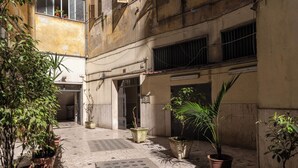 A courtyard with potted plants, a tiled floor, and a building entrance. - Timeless (Naples)