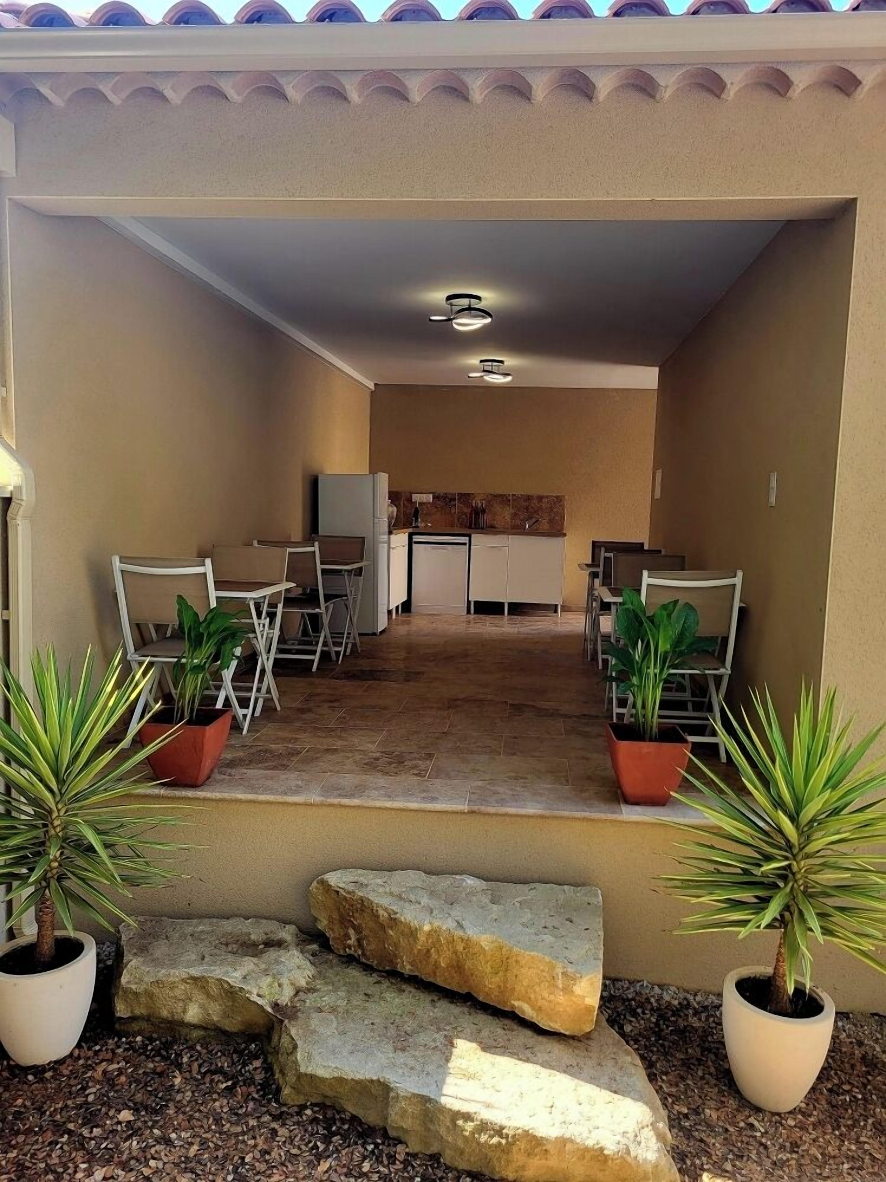 Un'area patio con tavolo e sedie, una piccola cucina sullo sfondo e piante in vaso.