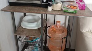 A kitchenette with a toaster oven, a water dispenser, a spice jar, a salt shaker, a plastic container with spices, and a pink bag. - Small Independent Studio in Zapopan (Zapopan)