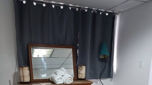 A bedroom with a wooden dresser, a mirror, a lamp, a trash can, and a bed with a blue cover. - Small Independent Studio in Zapopan (Zapopan)