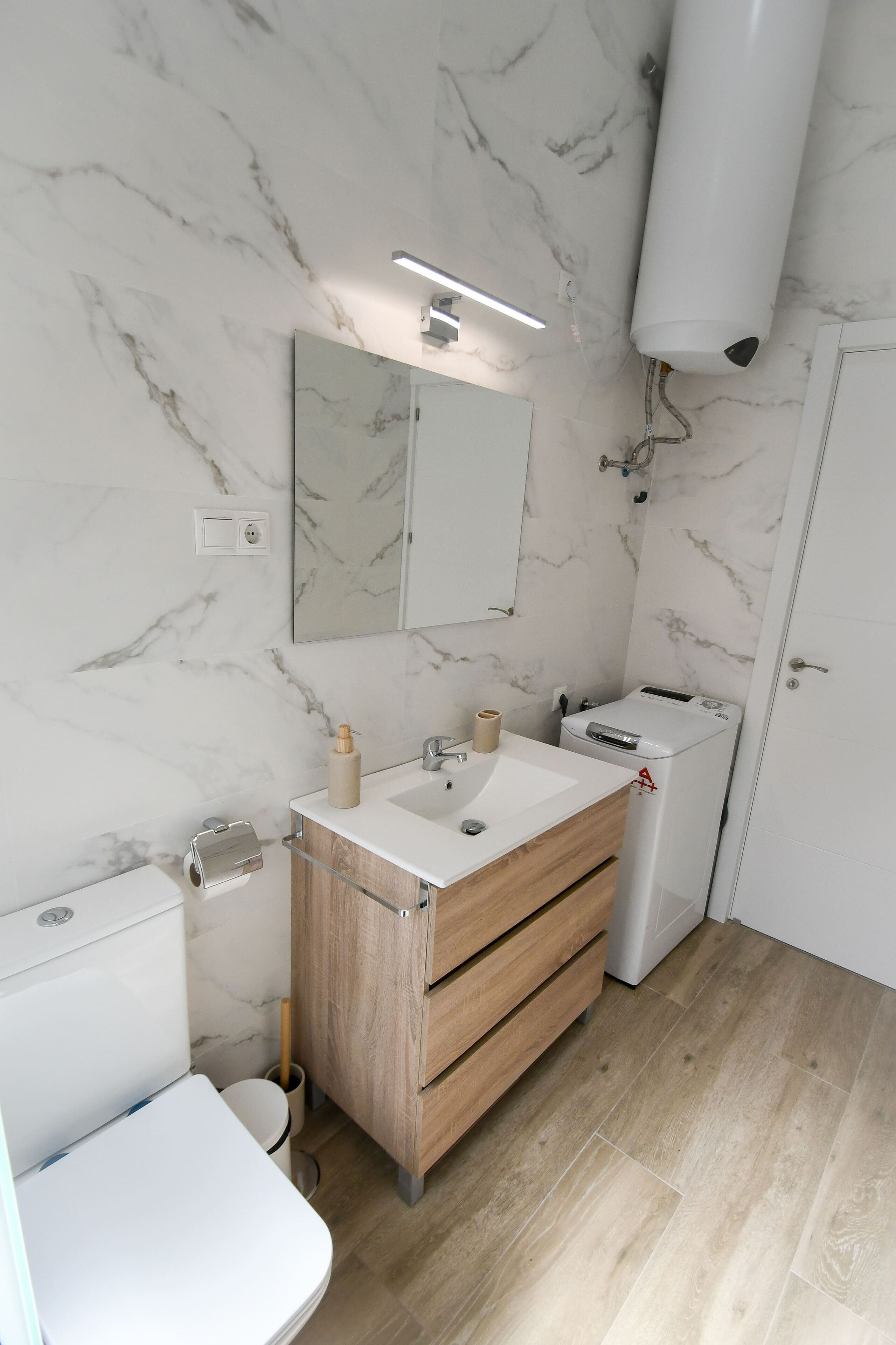 Un bany modern amb una paret de marbre, un moble de tocador de fusta, un vàter i un bidet.