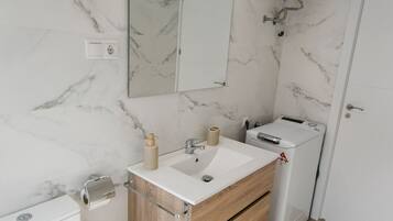Un bany modern amb una paret de marbre, un moble de tocador de fusta, un vàter i un bidet.