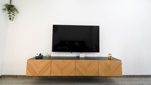 A modern living room with a flat-screen TV mounted on a white wall, a wooden cabinet below, and a small plant on the left.
