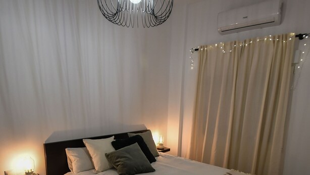 A neatly made bed with pillows, a bedside lamp, and a hanging light fixture.