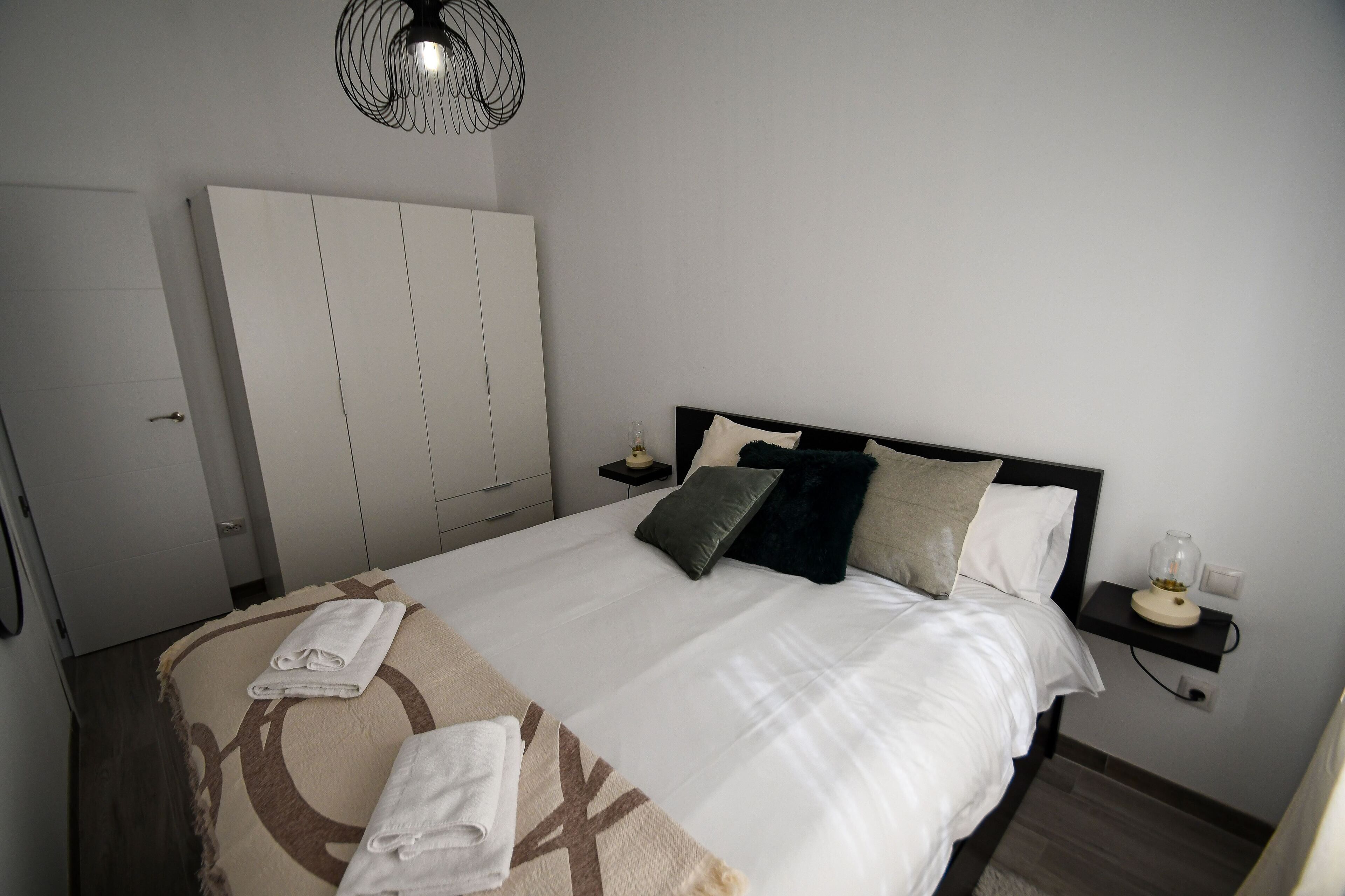 Una cama bien hecha con una colcha estampada, una mesita de noche con lámpara y un armario en una habitación de hotel.
