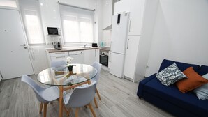 A modern kitchen with white cabinets, a microwave, and a stove. There is a dining table with chairs and a blue sofa with pillows.