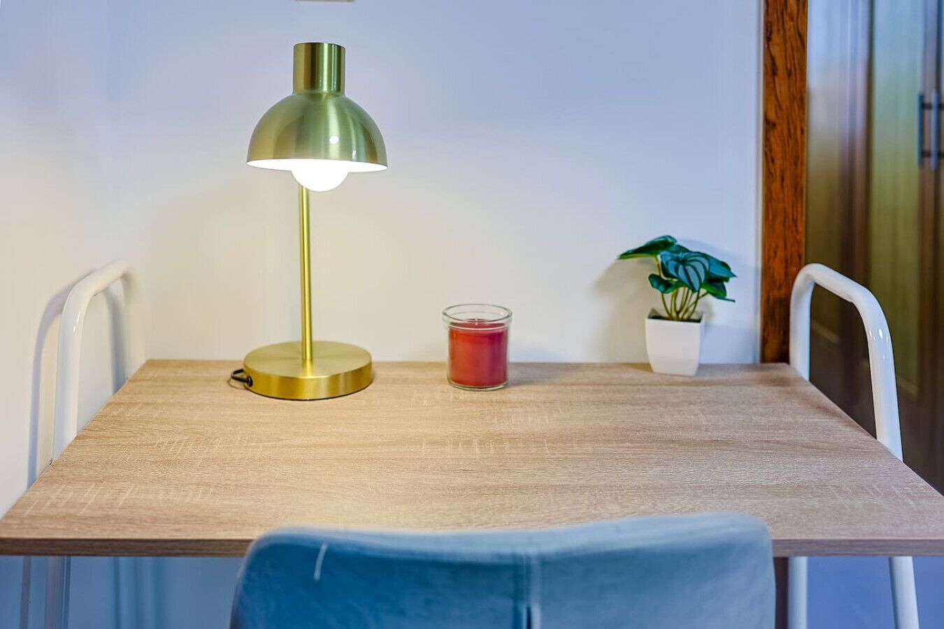 Une table en bois, une lampe de bureau verte, une bougie rouge et une plante en pot.