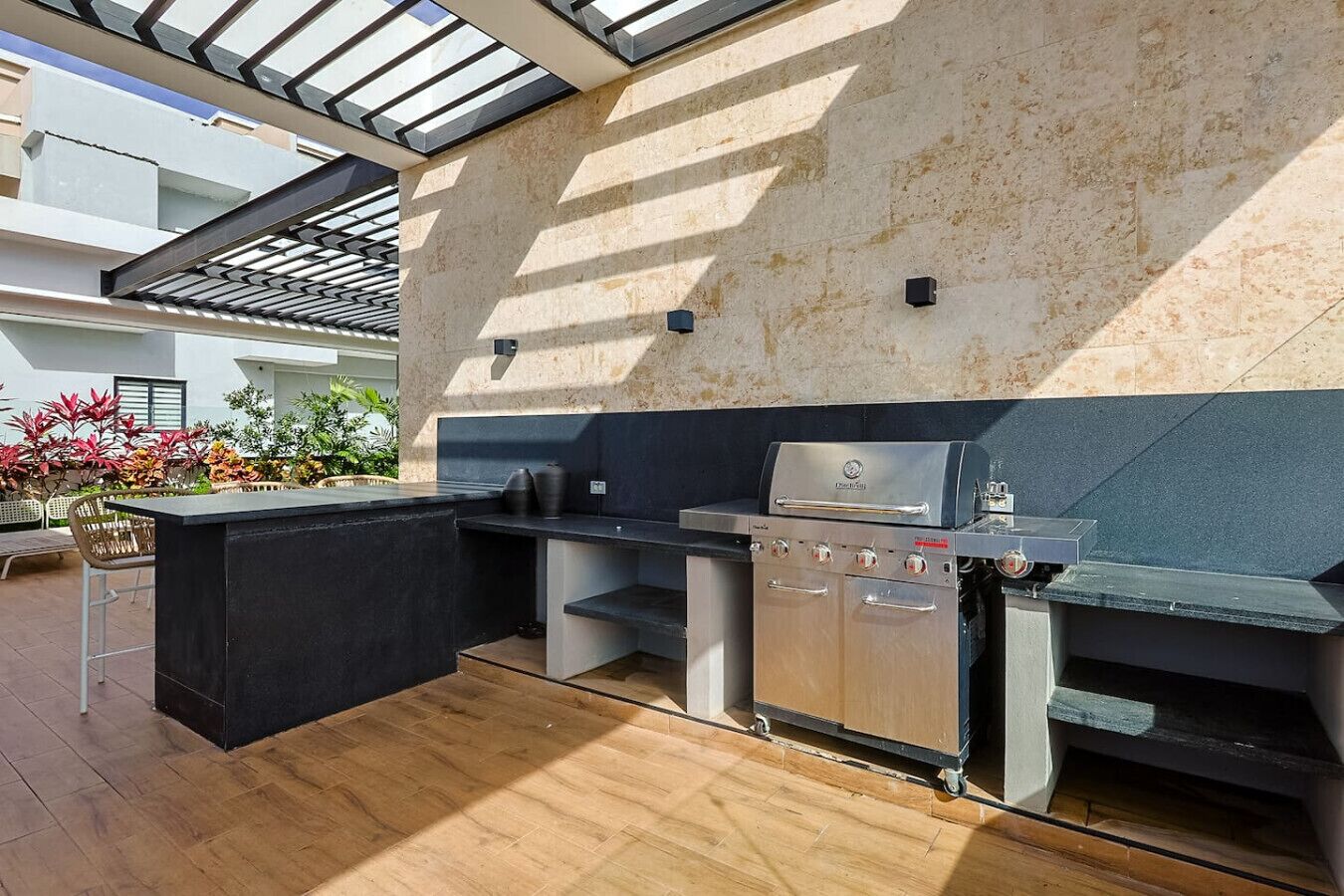 Un espace cuisine extérieur comprenant un barbecue, des tabourets de bar et une vue sur le jardin environnant.