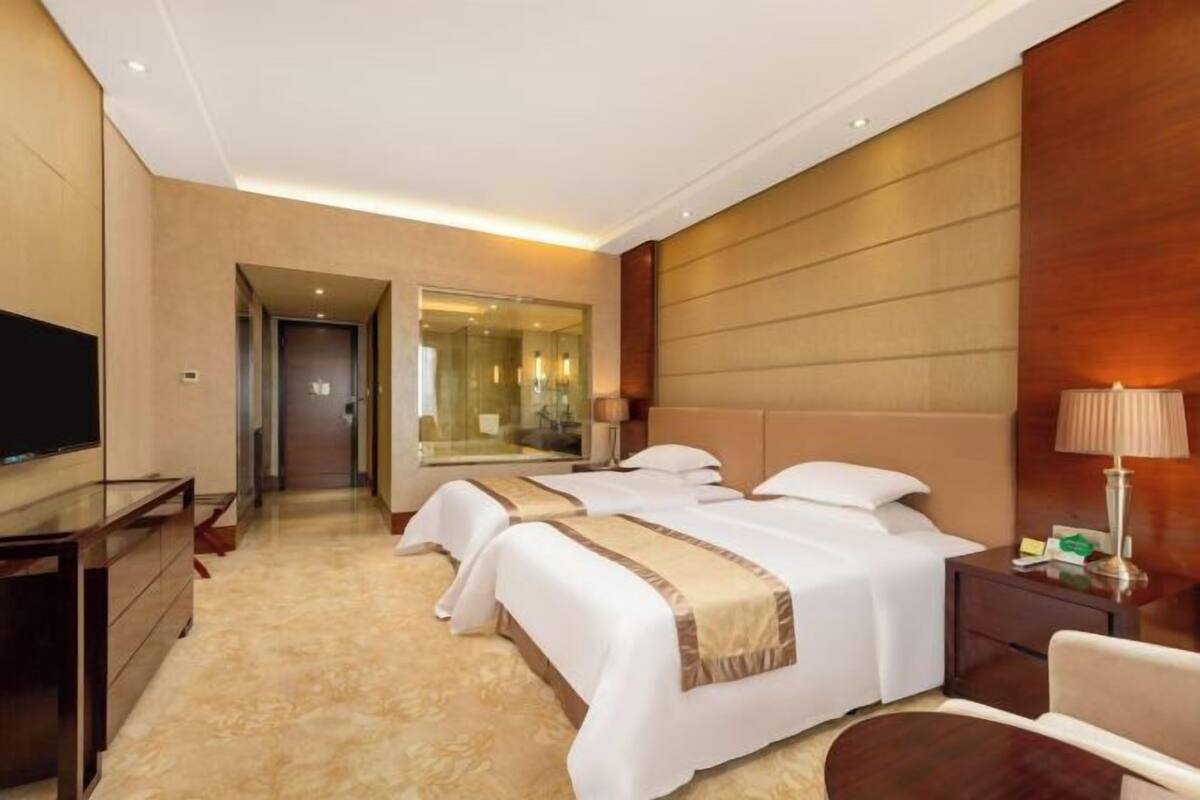 A hotel room with two beds, a TV, a desk, and a mirror.