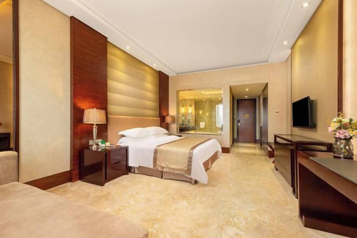 A hotel room with a bed, bedside tables, a TV, and a mirror.