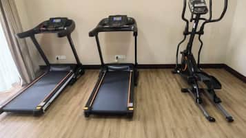Three exercise machines in a room with wooden flooring and a plain wall.