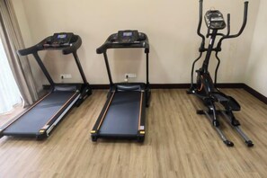 Drie fitnessapparaten in een ruimte met houten vloer en een effen muur.