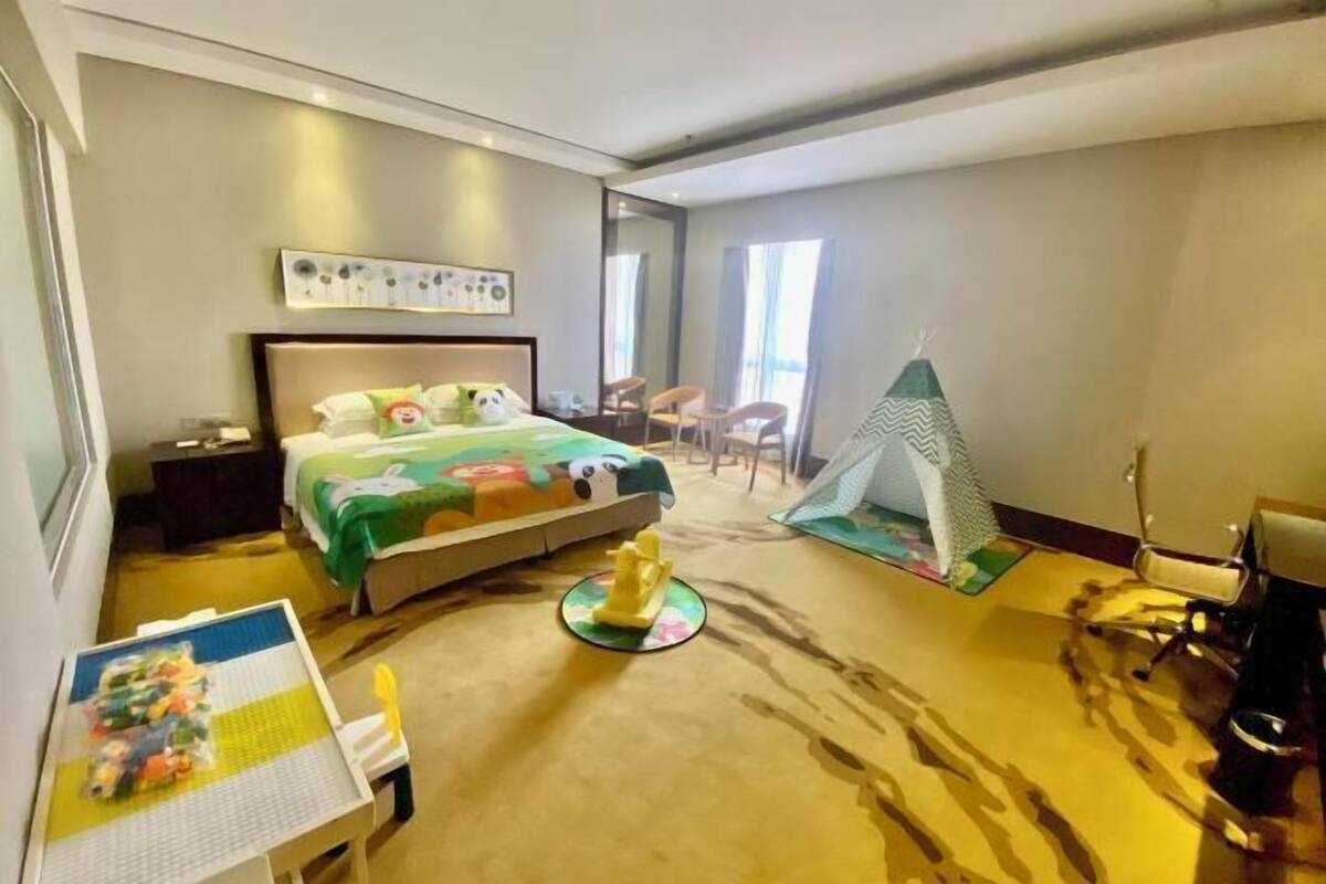 A hotel room with a bed, a play area with toys, a small tent, and a desk with a chair.