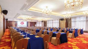 A conference room with rows of tables and chairs, a red carpet, and chandeliers.