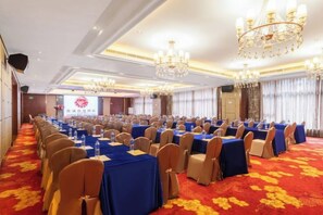 Une salle de conférence avec des rangées de tables et de chaises, une moquette rouge et des lustres.