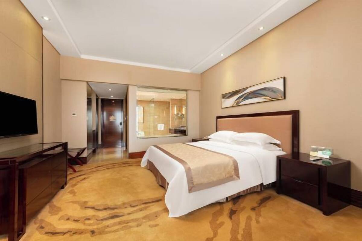 A hotel room with a large bed, a TV, a desk, and a carpeted floor.