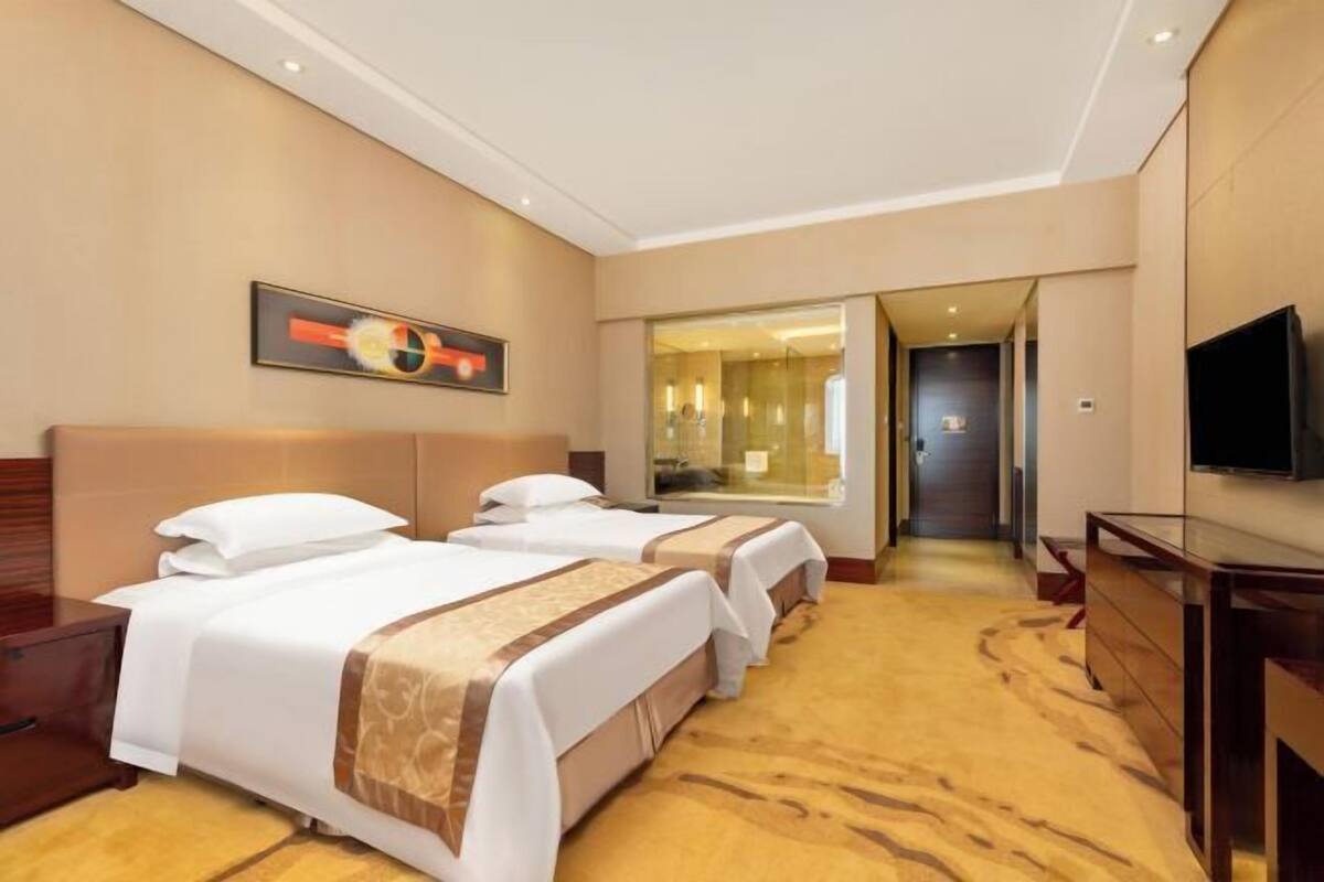 A hotel room with two beds, a TV, a mirror, and a hallway leading to a bathroom.