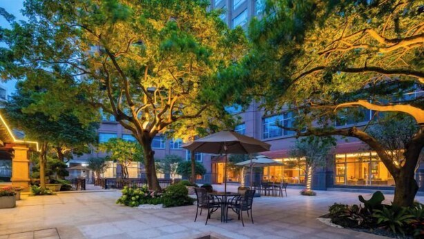 An outdoor patio area with tables and chairs, surrounded by trees and a building in the background. - Juncheng Higher-quarter Hotel (Zhongshan)