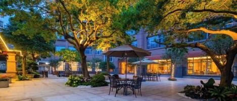 An outdoor patio area with tables and chairs, surrounded by trees and buildings.