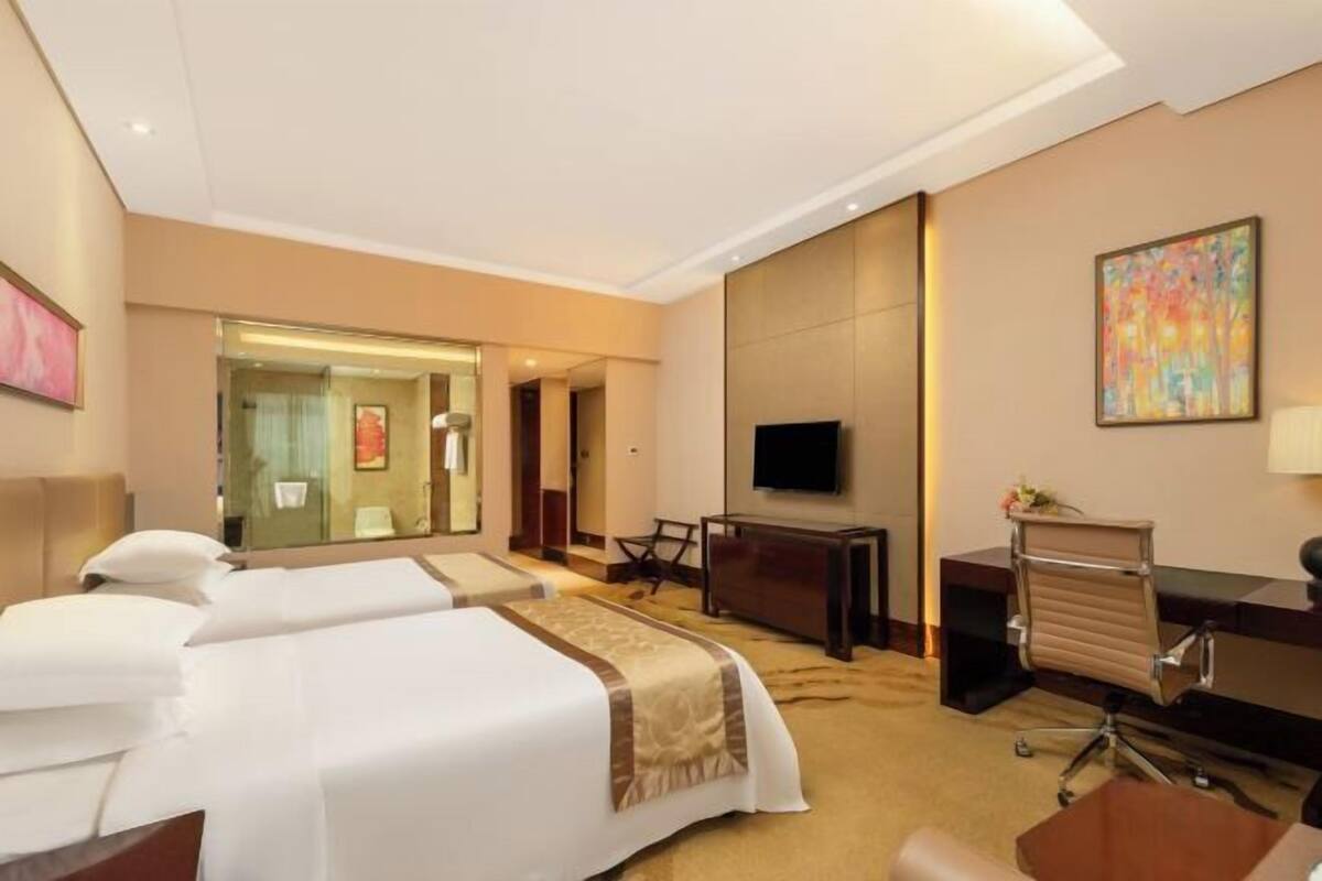 A hotel room with two beds, a desk, a TV, and a mirror.