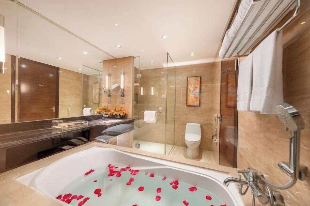 A modern bathroom with a glass-enclosed shower, a large bathtub with rose petals, and a vanity with a mirror and toiletries.
