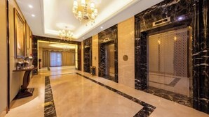 A spacious hotel lobby with marble flooring, a chandelier, and a modern elevator. - Juncheng Higher-quarter Hotel (Zhongshan)