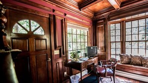 A room with a wooden door, a desk with a computer, a chair, and a window with a view of trees.