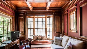 A room with a wooden desk, a leather chair, a sofa, and a bay window with a view of greenery.