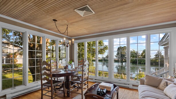 Une pièce spacieuse avec de grandes fenêtres, un plafond en bois, un coin repas avec une table et des chaises, et une vue sur un lac.