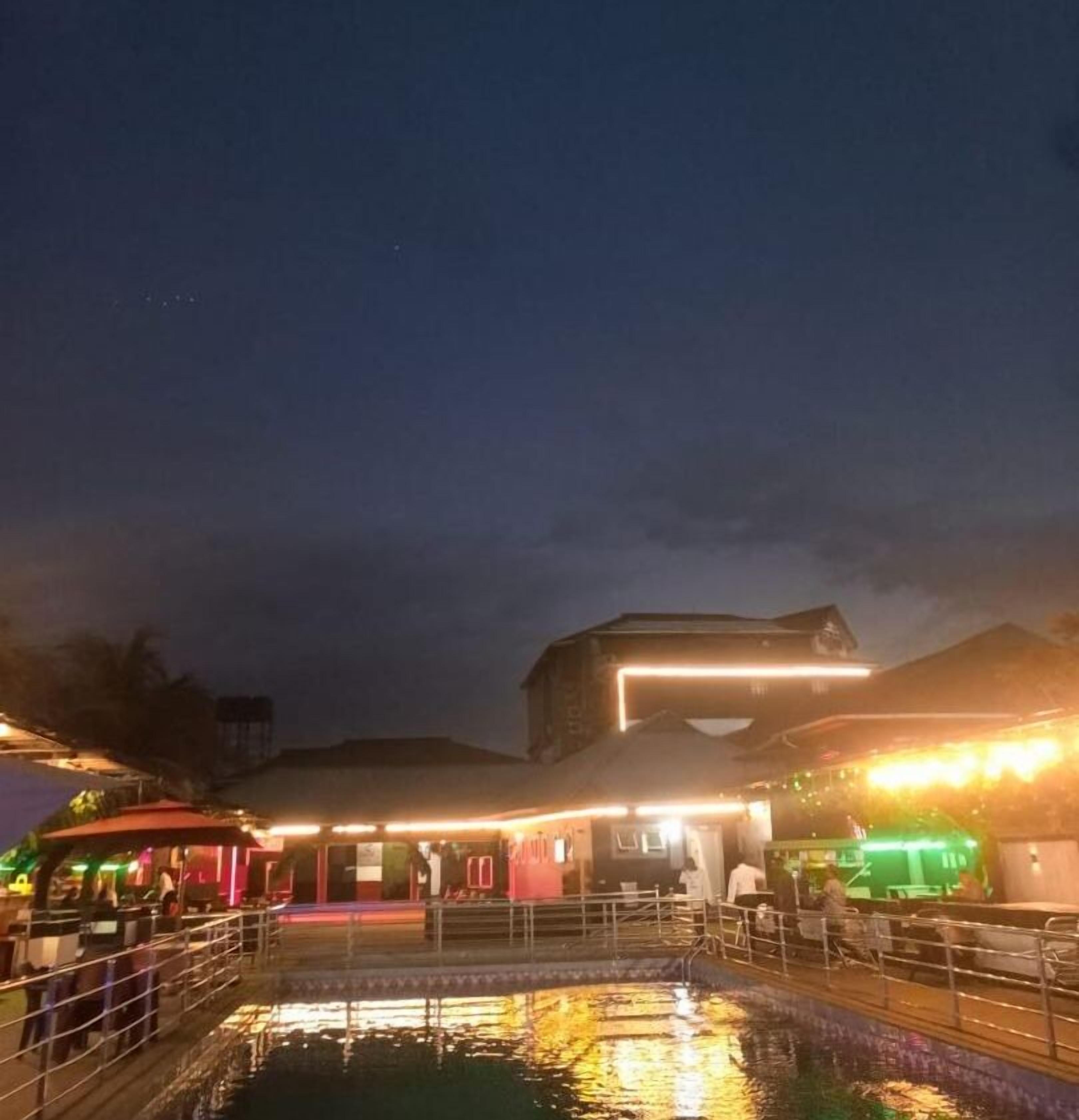 A waterfront hotel with a pool, outdoor seating, and illuminated structures.