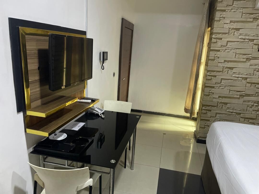 Une chambre d’hôtel comprenant un lit, un bureau avec une chaise, un téléviseur à écran plat, un téléphone et un mur à la texture de pierre.