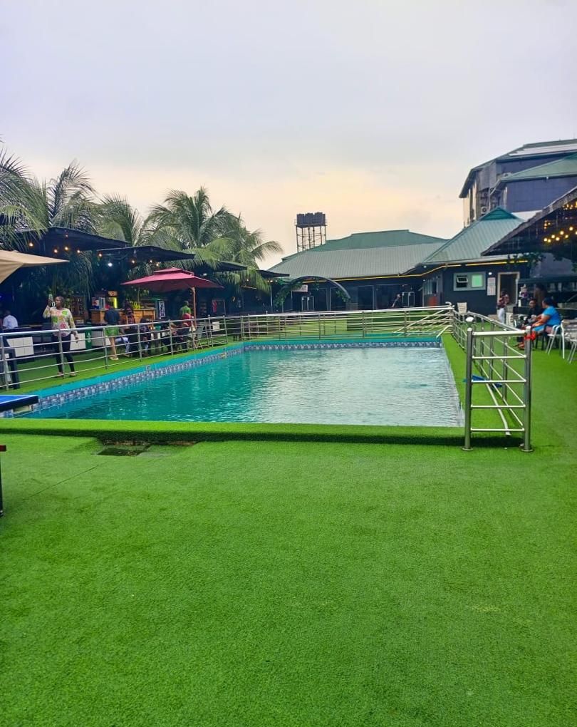 Une piscine entourée d’une pelouse verdoyante, délimitée par une clôture et ombragée par des parasols.