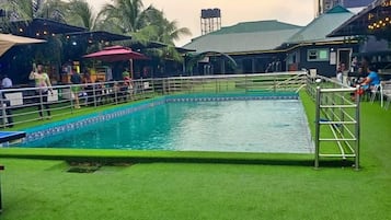 Une piscine entourée d’une pelouse verdoyante, délimitée par une clôture et ombragée par des parasols.