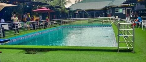 Una piscina con un borde circundante, palmeras y un edificio con techo verde.