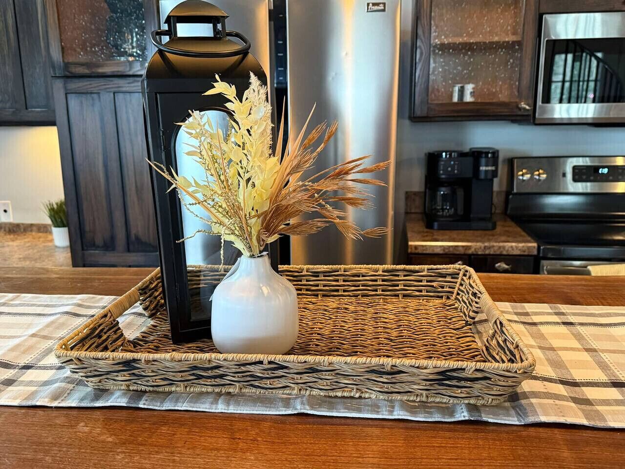 A kitchen counter with a woven tray holding a vase of dried flowers and a black lantern.