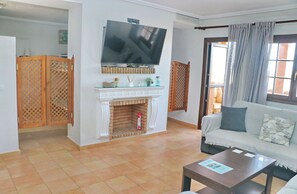 A living room with a fireplace, a television mounted above it, a sofa with cushions, and a table with a magazine.